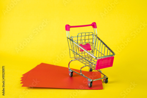 Shopping cart or supermarket trolley and blank red envelop on yellow background with space for add text, Chinese new year and shopping concept.