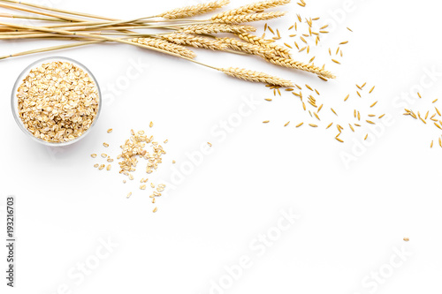 Cereals concept. Oatmeal in bowl near sprigs of wheat on white background top view copy space