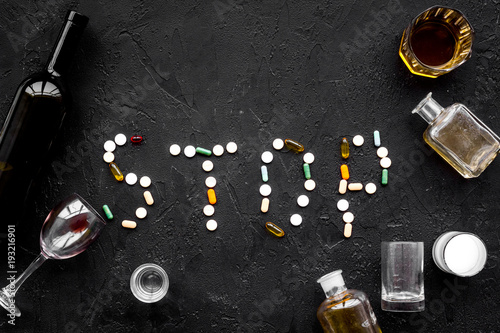 Stop alcohol. Word stop lined with pills near glasses and bottles on black background top view copy space