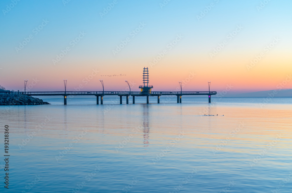 Birds flying over modern pier during pastel colored sunrise