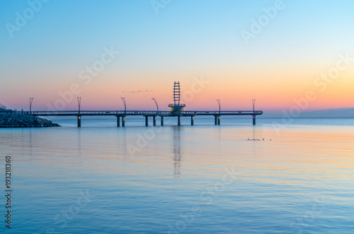 Birds flying over modern pier during pastel colored sunrise