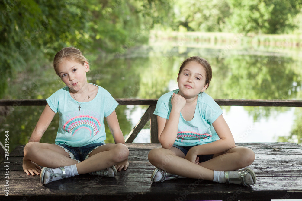 Two girls are sitting on a wooden table in front of a lake Two girls are sitting on a wooden table in front of a lake