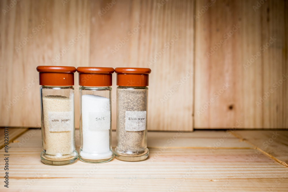 Concept of salt, black and white pepper powder accessories. Bottles with salt, black and white pepper on wooden background. Horizontal. Concept of salt, black and white pepper powder accessories. Bottles with salt, black and white pepper on wooden background. Horizontal.