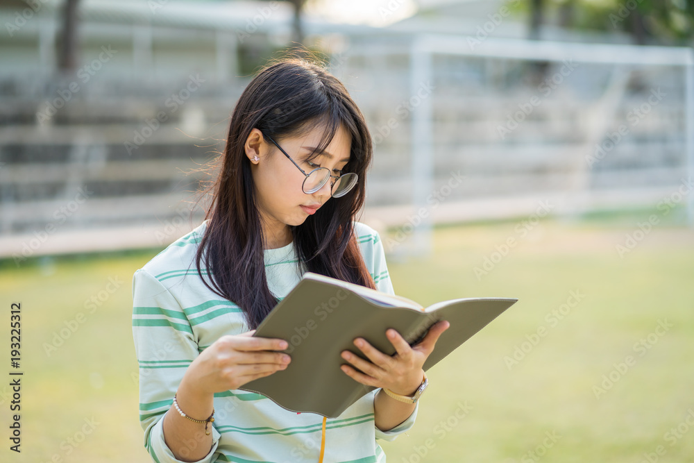 Obraz premium Teenage girl wearing eyeglasses standing Read a notebook in football field at sunset