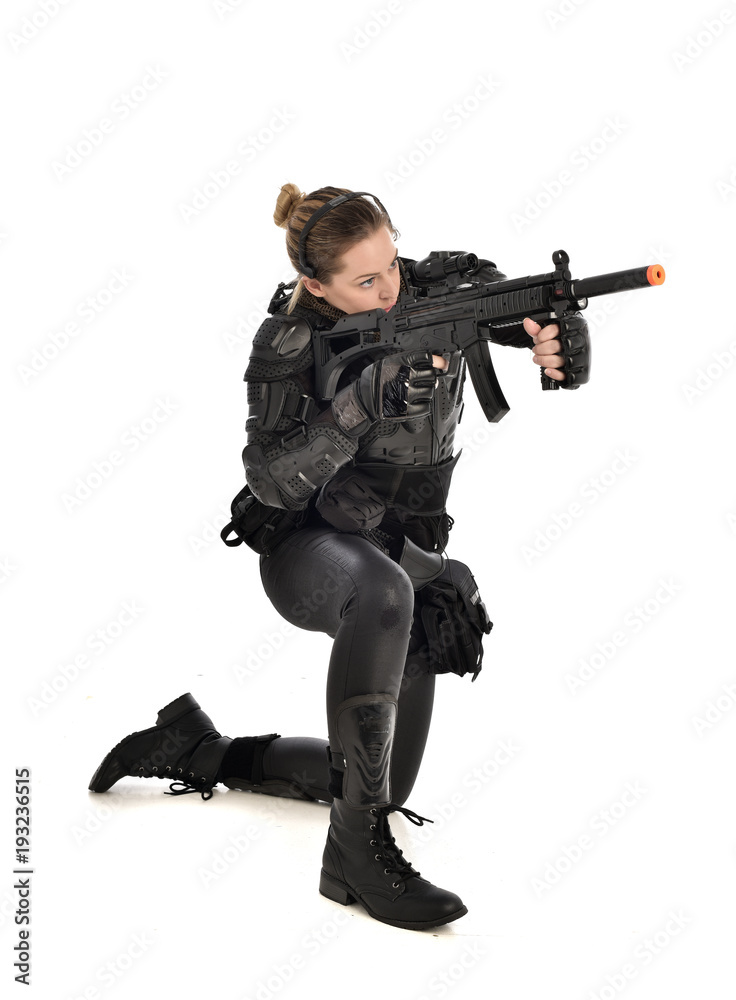 full length portrait of female wearing black tactical armour, crouching pose holding a weapon, isolated on white studio background. full length portrait of female wearing black tactical armour, crouching pose holding a weapon, isolated on white studio background.