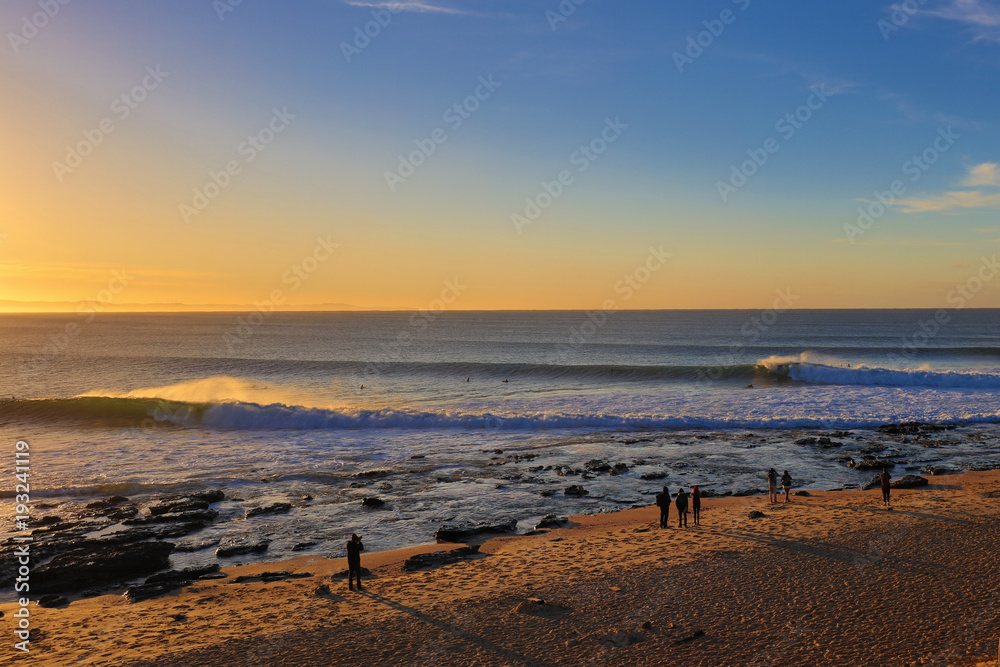 Sunrise at the beach in Jeffreys Bay, South Africa. There are surfers having fun in the waves with a few people on the beach