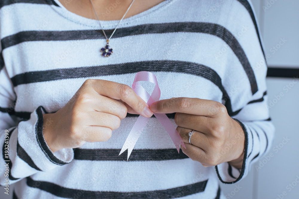 Woman hand holding pink ribbon of breast cancer struggle symbol