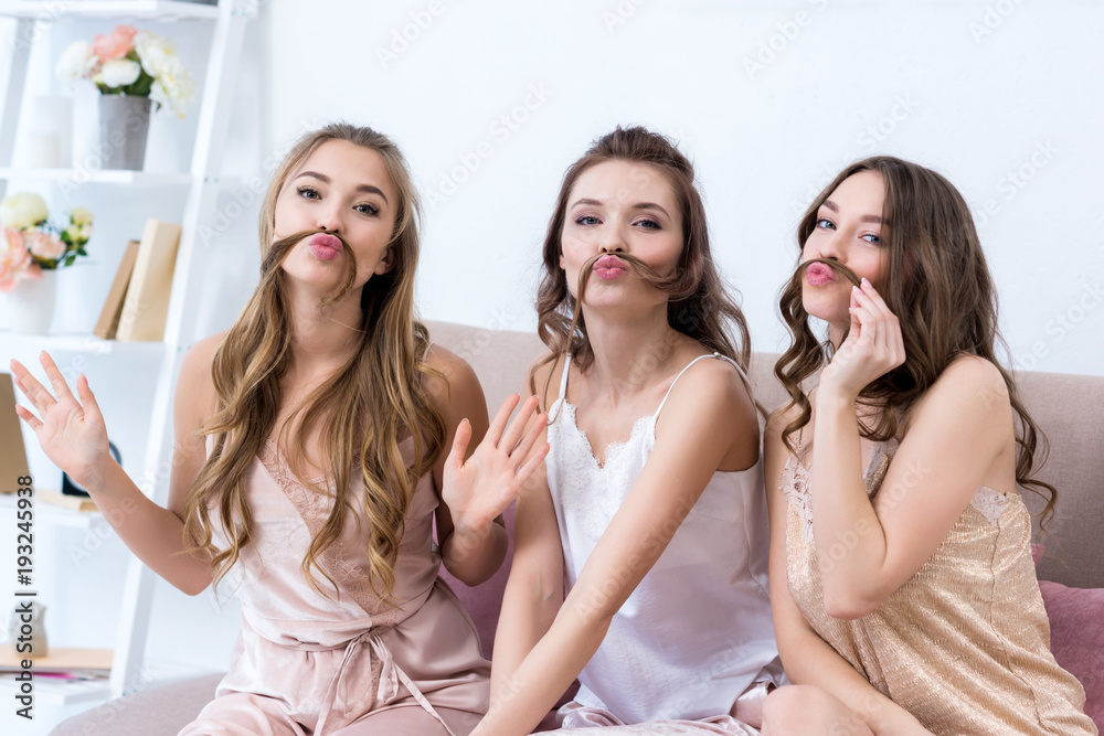 beautiful young women in pajamas holding hair as moustaches and smiling at camera beautiful young women in pajamas holding hair as moustaches and smiling at camera