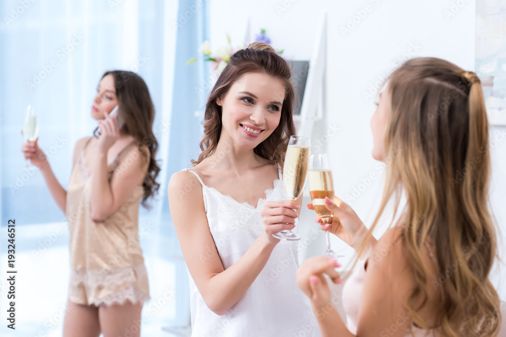 beautiful young women in pajamas drinking champagne while friend talking by smartphone beautiful young women in pajamas drinking champagne while friend talking by smartphone