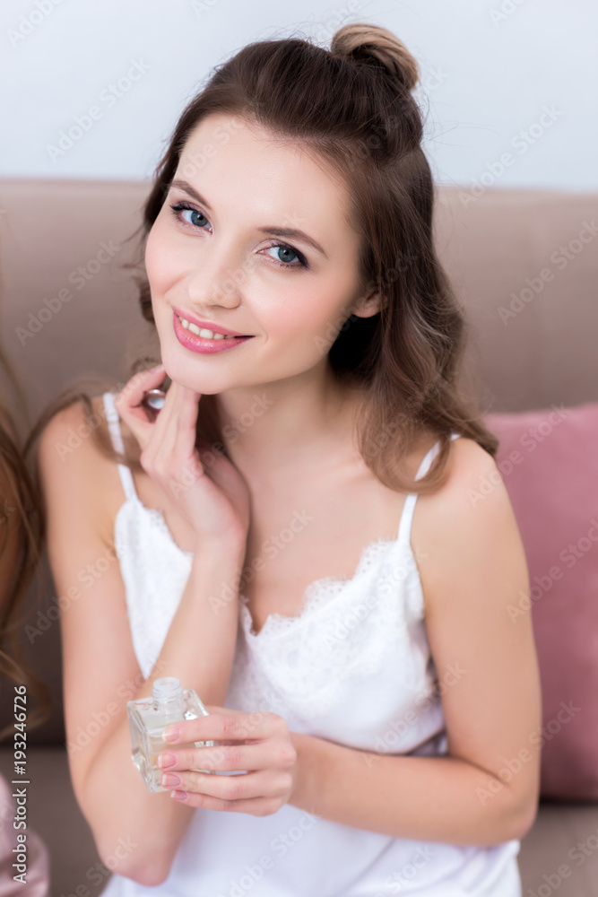 beautiful young woman holding bottle of perfume and smiling at camera beautiful young woman holding bottle of perfume and smiling at camera
