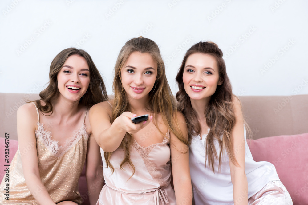 beautiful young women in pajamas using remote controller and smiling at camera beautiful young women in pajamas using remote controller and smiling at camera
