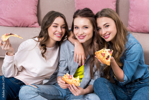 beautiful young women eating pizza and smiling at camera
