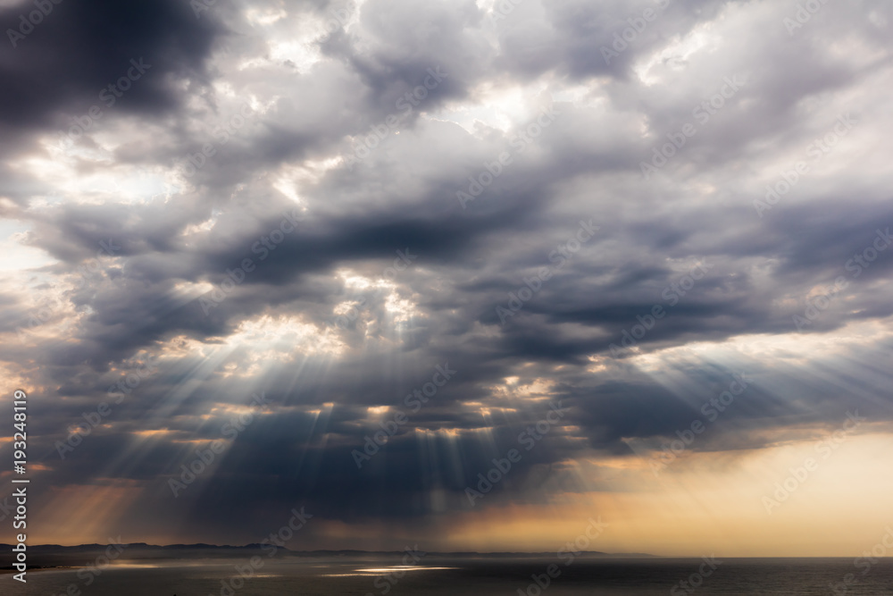 Spectacular cloud formation with broken dark clouds and the sun rays shining through gaps craeting highlights on the sea