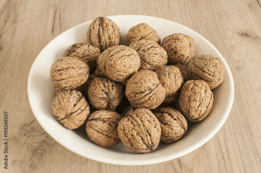 A pile of whole orgranic walnuts in shell closeup in porcelain bowl A pile of whole orgranic walnuts in shell closeup in porcelain bowl