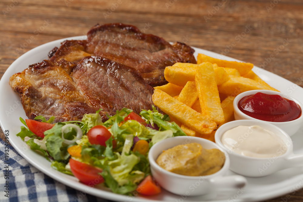 Grilled pork neck served with French fries and salad. Grilled pork neck served with French fries and salad.