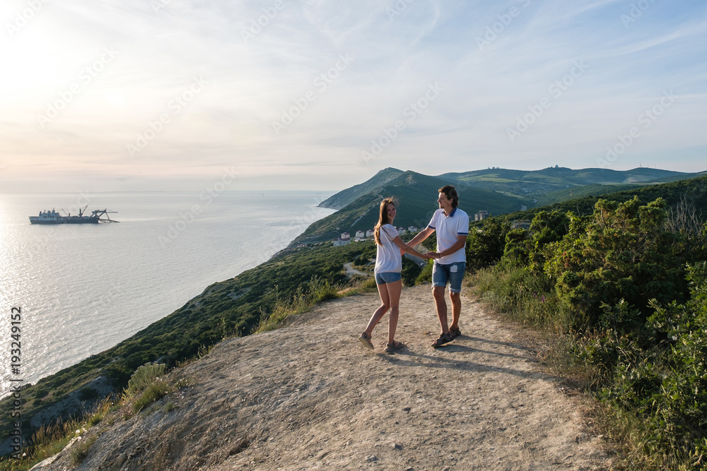 Couple happy man and woman walking on a country road in the mountains with seascape. Front view.