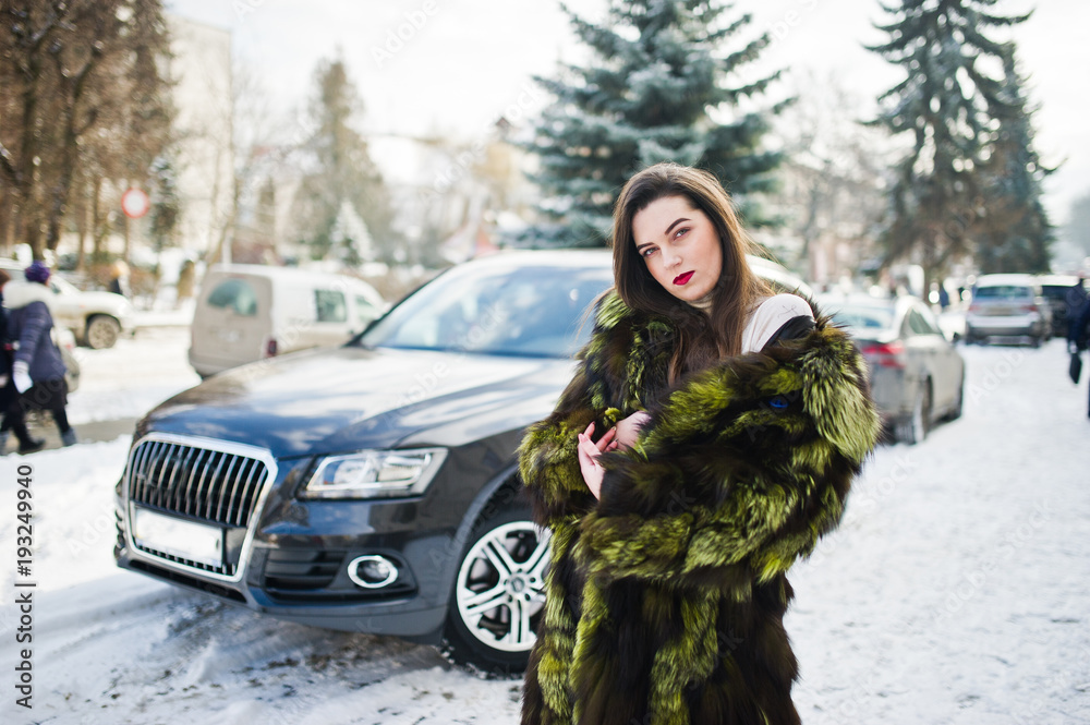 Brunette girl in green fur coat at street of city background car in winter day.