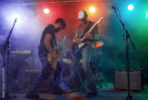 Rock band performs on stage. Guitarist, bass guitar and drums.