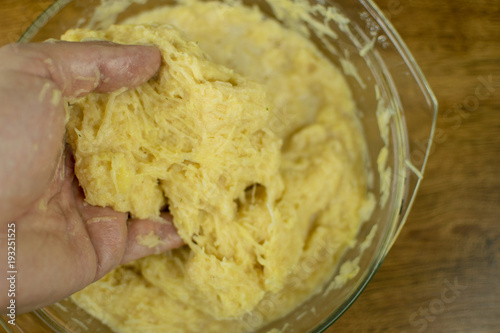 The hand is kneading grated potatoes to make dough.