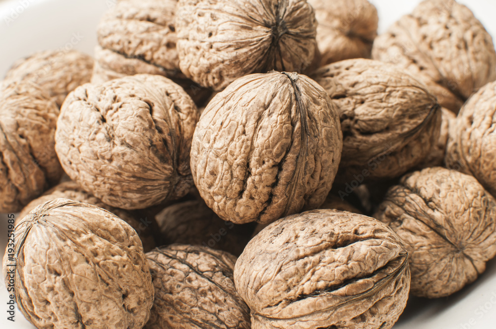 A pile of whole orgranic walnuts in shell closeup in porcelain bowl A pile of whole orgranic walnuts in shell closeup in porcelain bowl