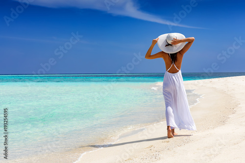 Elegante Frau in weiß läuft über einen tropischen Strand und genießt ihren Urlaub photo