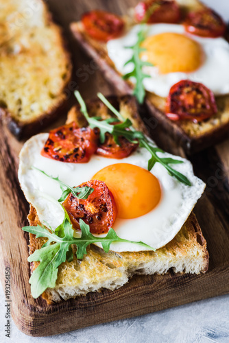 Breakfast toast with egg, roasted tomatoes and arugula salad. Closeup view