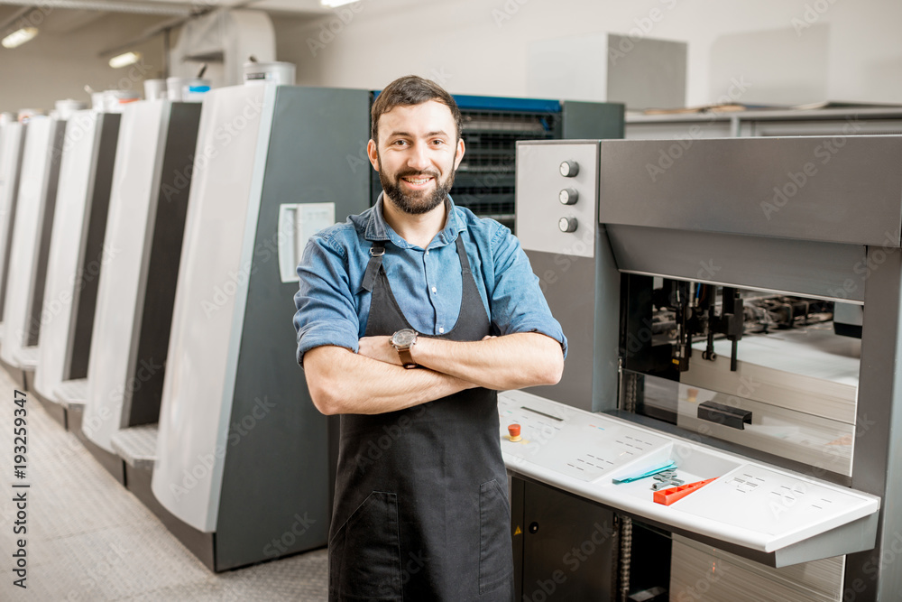 Portrait of a handsome typographer standing at the printing manufacturing with offset machine on the backgorund Portrait of a handsome typographer standing at the printing manufacturing with offset machine on the backgorund