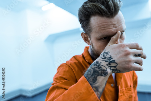 tattooed prisoner covering face with hand