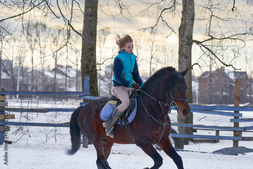 A girl on a horse jumps gallops. A girl trains riding a horse in a small paddock. A cloudy winter day.