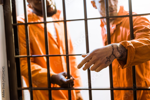 Φωτογραφία multicultural prisoners standing near prison bars in prison cell
