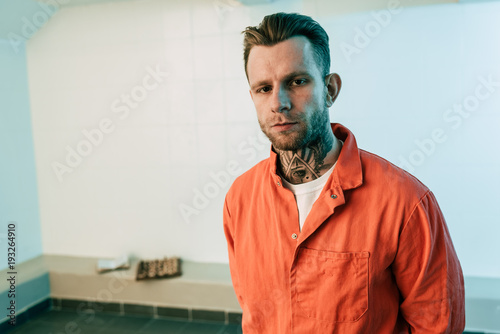 Fotografering tattooed prisoner looking at camera in prison cell