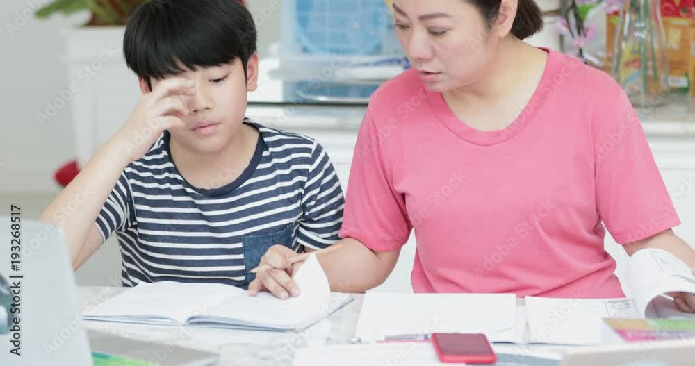 Serious Asian mother with son doing homework in the living room. Mom teaches son how to genius. Serious Asian mother with son doing homework in the living room. Mom teaches son how to genius.
