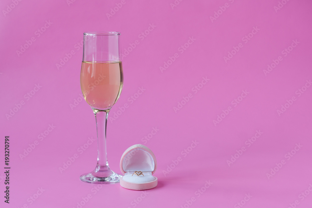 Engagement ring and glass of wine on pink background. Space for text