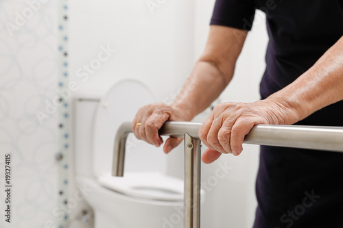 Elderly woman holding on handrail in bathroom. Fototapet