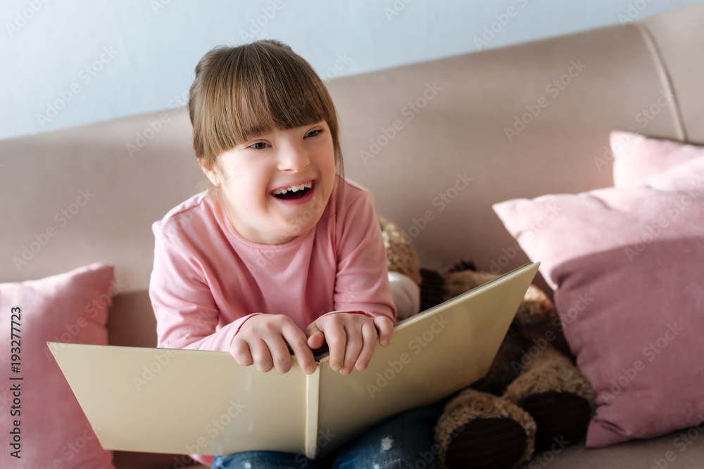 Kid with down syndrome holding book and laughing