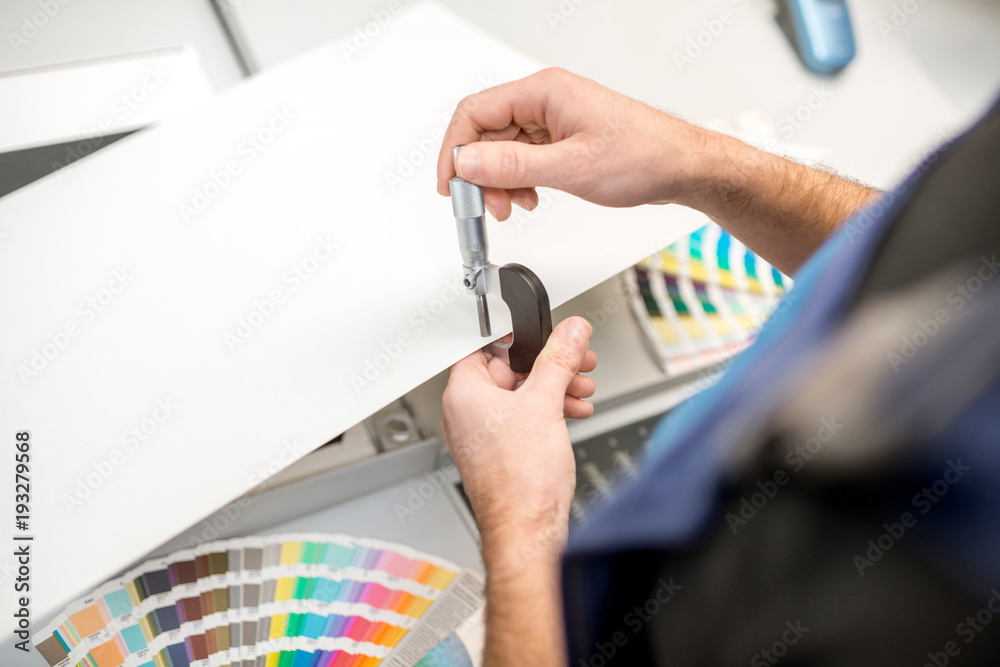 Man measuring thickness of the paper sheet with micrometer at the printing plant Man measuring thickness of the paper sheet with micrometer at the printing plant