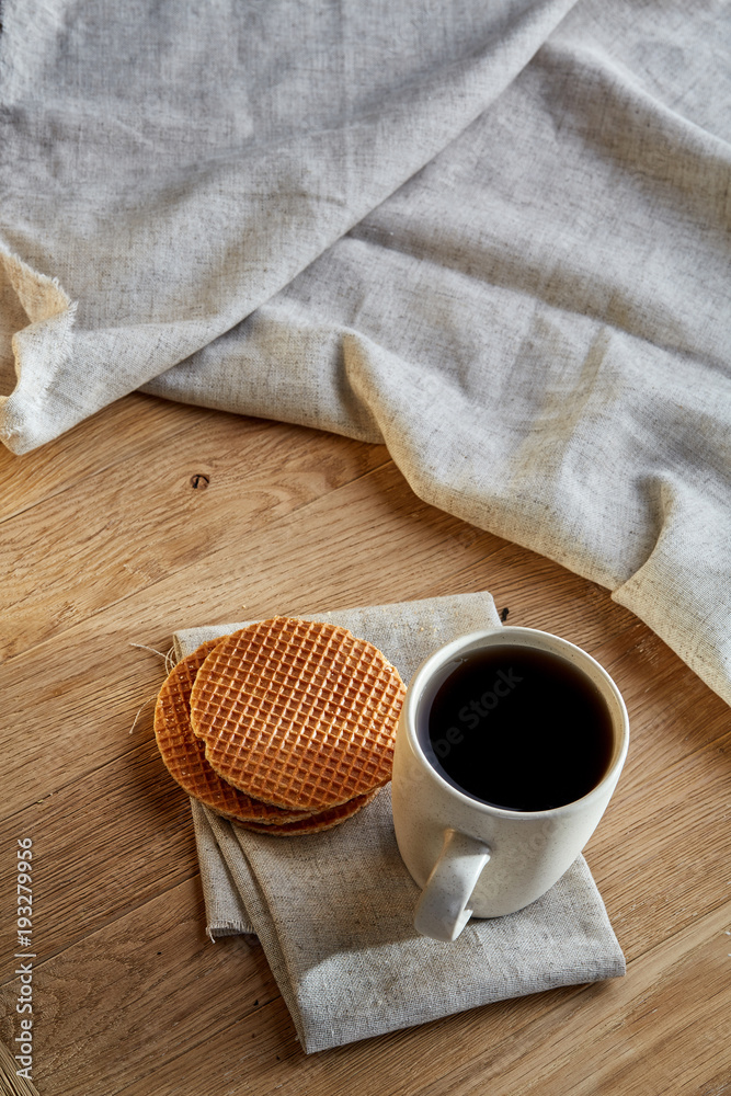 Porcelain teacup with waffles on cotton napkin on a rustic wooden background, top view, vertical Porcelain teacup with waffles on cotton napkin on a rustic wooden background, top view, vertical