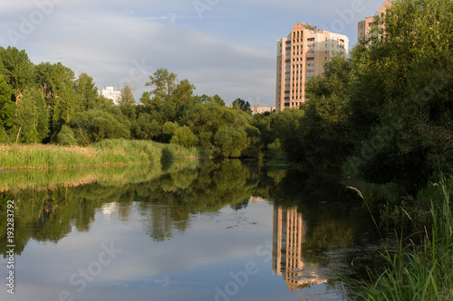 Beautiful summer embankment. Mirror reflection of a summer park in the water's surface. Warm summer day.