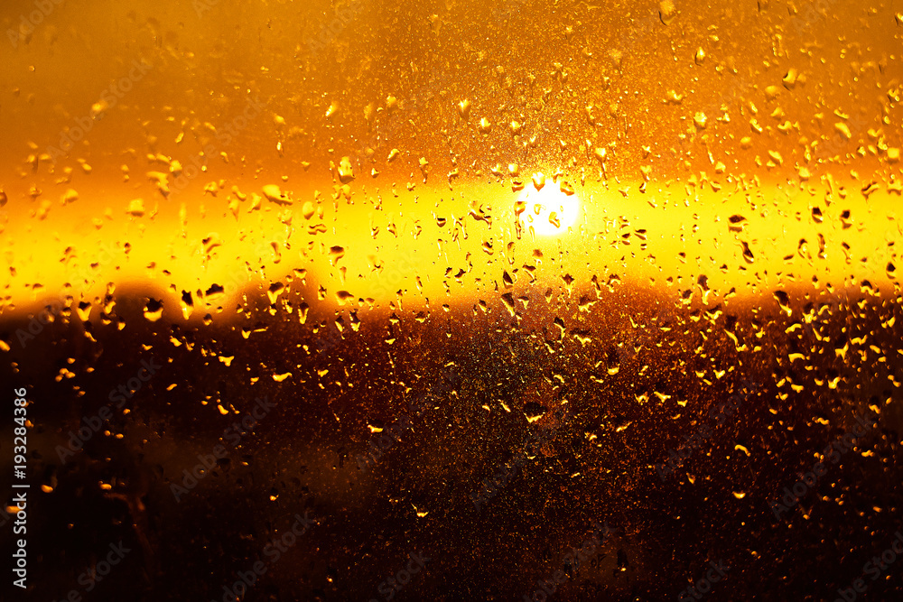 Rain drops texture on window glass with gorgeous colorful orange amber sunset light abstract blurred cityscape skyline bokeh background. Soft focus.