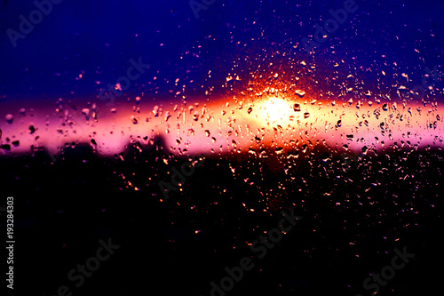 Rain drops texture on window glass with stunning colorful violet pink sunset light abstract blurred cityscape skyline bokeh background. Soft focus.