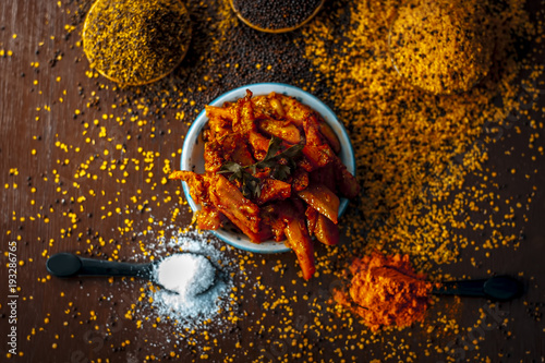 Close up of popular Indian cucumber pickle with all its ingredients including spices and herbs on a wooden surface in dark Gothic colors. photo