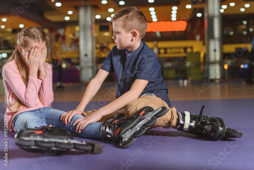 brother cheering up crying sister in roller skates on roller rink