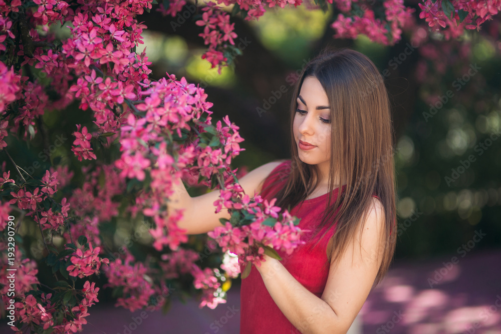 Beautiful girl posing to the photographer against the background of blooming pink trees. Spring. Sakura Beautiful girl posing to the photographer against the background of blooming pink trees. Spring. Sakura
