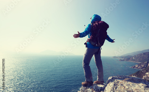 successful female hiker stand on sunrise seaside mountain cliff edge