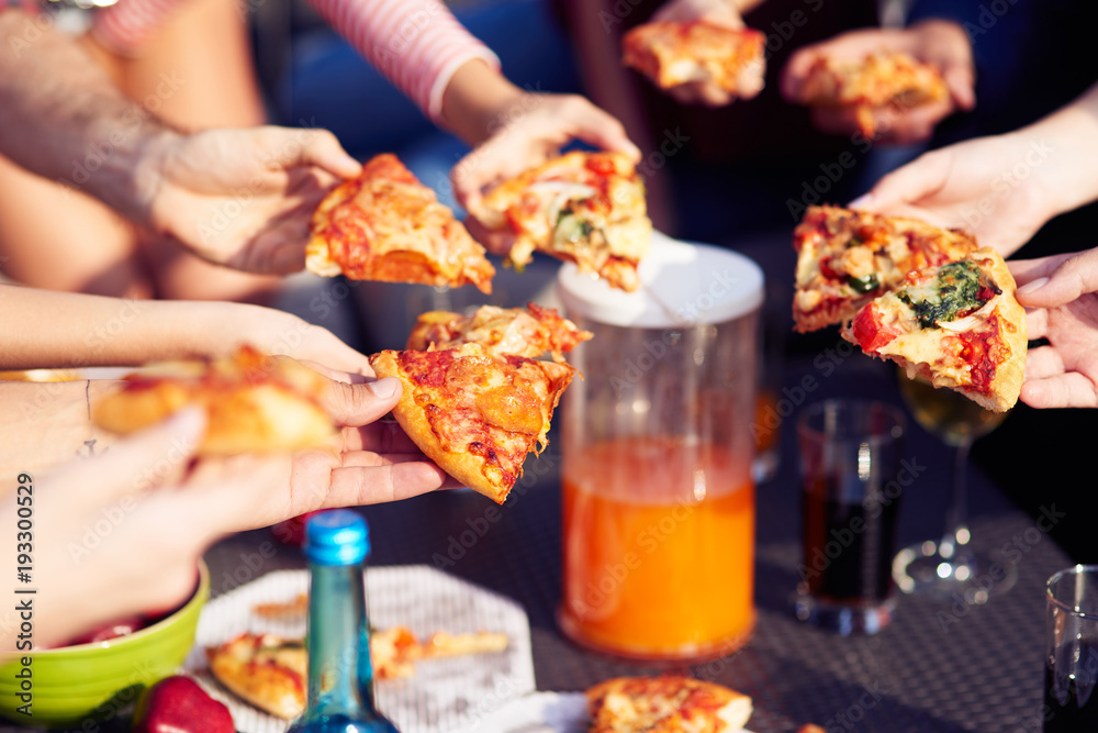 Close up of pizza pieces in hands of friends