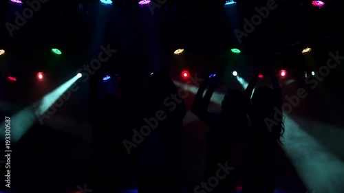 Three sexy girls and one guy dancing at the party in the dark in the light colored lights. Slow motion. Silhouette.