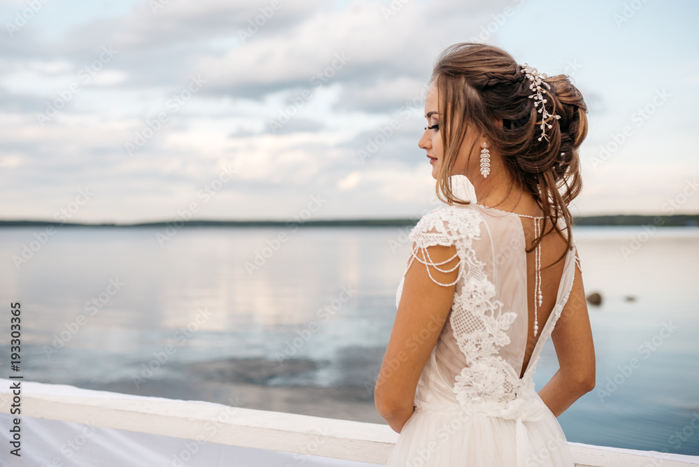 A beautiful bride is standing on the pier. Water surface and cloudy sky on the background A beautiful bride is standing on the pier. Water surface and cloudy sky on the background