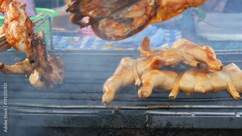 Whole chicken carcass grill strung on wooden stick grilling on the grill. Street Food Thailand. Men's hands turn over the grilled chicken photo