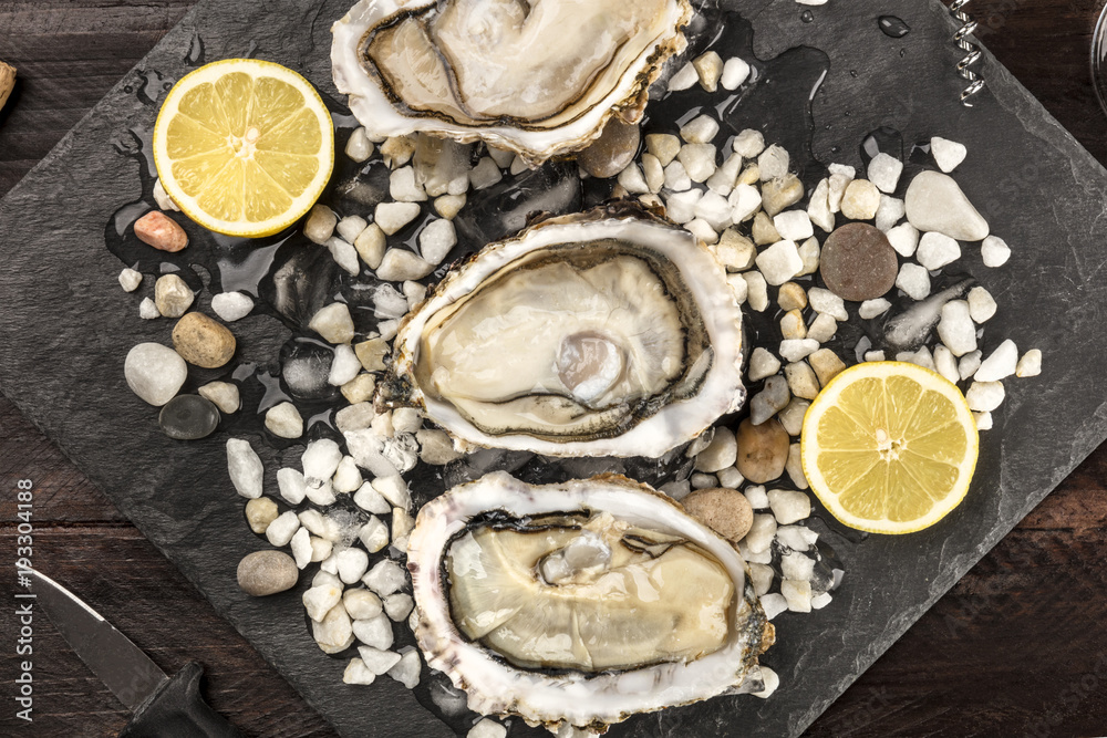 Overhead closeup photo of shucked oysters on dark textures Overhead closeup photo of shucked oysters on dark textures
