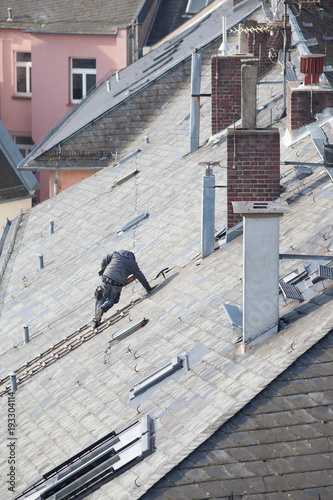 Roofer repairs shingle on rooftop